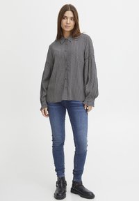 Camicia a maniche lunghe con motivo bianco e nero, abbinata a jeans blu aderenti e stivaletti neri. Tessuto dalla texture liscia.
