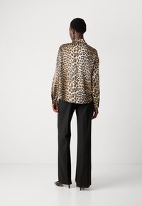 Leopardprint silke bluse med høj krave og lange ærmer, parret med sorte vidde bukser. Glat tekstur og markante mønsterdetaljer.