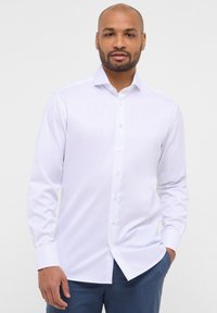 Camicia button-up bianca a righe con maniche lunghe, tessuto morbido e colletto a camicia. Presenta un orlo dritto e bottoni bianchi classici.