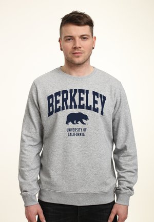 Šedá mikina s kulatým výstřihem, s modrým nápisem "BERKELEY" a grafikou medvěda, označená "Univerzita Kalifornie". Dlouhé rukávy.