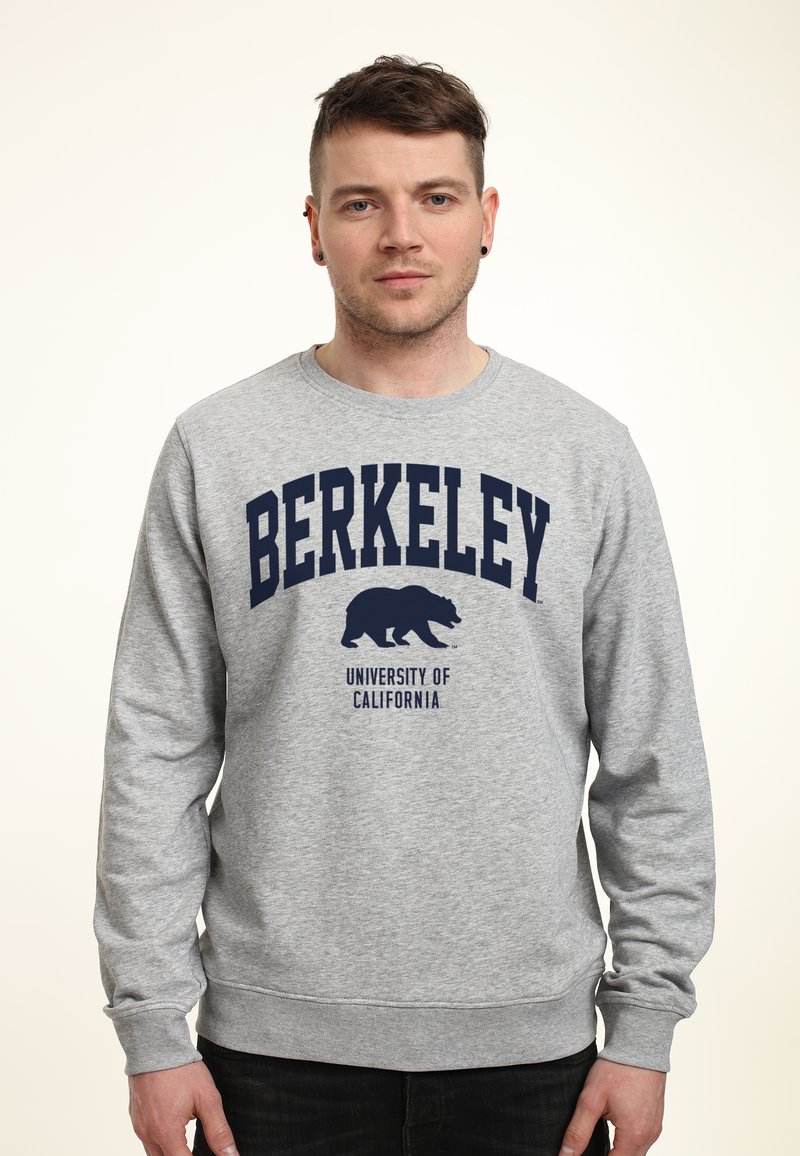 Šedá mikina s kulatým výstřihem, s modrým nápisem "BERKELEY" a grafikou medvěda, označená "Univerzita Kalifornie". Dlouhé rukávy.