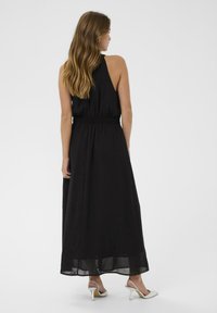 Sort maxikjole med halterneck, smocket talje og luftig stof. Har et gennemsigtigt nederste lag og sølvfarvede hæle.