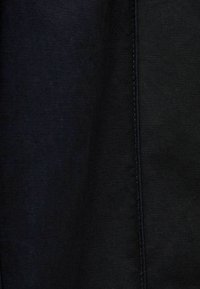 Mustat denim-kangas, joka esittelee sileää rakennetta ja hienovaraista kiillettä. Edessä pystysuora vahvistettu sauma.