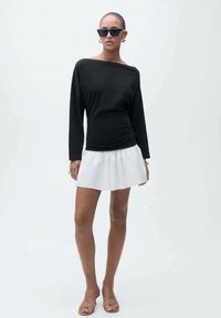 Črn off-shoulder dolg rokav top, vparen z belim razširjenim mini krilom in bež sandali, z gladko teksturo in minimalističnim stilom.