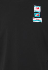 Černé tričko vyrobené z bavlny, které obsahuje tři barevné nášivky s textem a logy "New Balance". Kulatý výstřih a krátké rukávy.