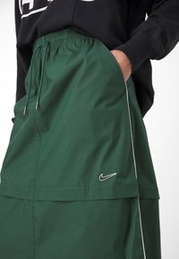 Grön Nike-kjol med elastisk midja, sidofickor och vit piping. Har en liten svart logotyp i nedre högra hörnet. Slät textur.