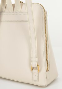 Sac à main en cuir couleur crème avec une texture lisse, fermeture éclair dorée et poignées robustes. Présente un design fin et structuré avec des coutures subtiles.