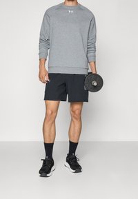 Sweatshirt gris avec col rond, shorts noirs, chaussures de sport noires, et une plaque de poids tenue à la main ; tenue décontractée pour des activités de fitness.