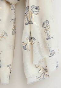 Balts šalle ar teksturētu audumu, kurā ir zilu kokteiļu glāžu un metālisku zelta lentīšu raksts. Frizētie mali piešķir detaļu.