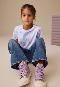 Tricou grafic pentru tineret cu design de fluture în culori pastel, asortat cu blugi denim cu picioare largi și adidași cu platformă înaltă și sclipici multicolor.