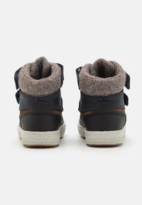 Høye sko i svart lær med brune detaljer og en grå filtkrage. Har to justerbare stropper og en hvit gummisåle.