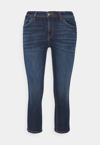 Jeans de mezclilla azul oscuro con un corte ajustado, cinco bolsillos y cremallera. La costura es visible, con un ligero desvanecimiento y puños rematados.