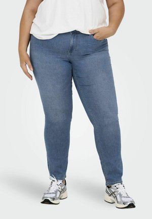 Modré džíny skinny s hladkou textúrou a jemným elastickým materiálom, s médium vzostúpeným pásom a dizajnom piatich vreciek. Skombinované s bielymi teniskami.
