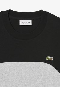 Camiseta de manga corta en negro y gris con un cuello redondo acanalado, que presenta un pequeño logo de cocodrilo verde en el pecho. Diseño de corte clásico.