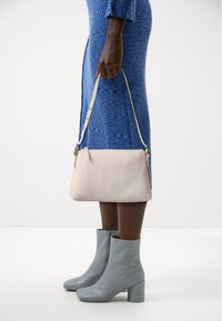 Beige Lederhandtasche mit verstellbarem Tragegurt, glatte Textur, rechteckige Form. Kombiniert mit einem blauen, strukturierten Kleid und hellblauen Absatzstiefeln.