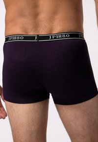 Pantalones cortos de boxeo en tejido púrpura oscuro con una cinturilla elástica negra que presenta "JP1880" en letras blancas, mostrando un diseño liso y ajustado.