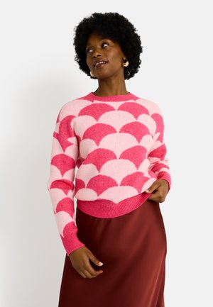 Suéter de punto con un patrón de borde de concha en rosa y rosa claro, cuello redondo, puños y dobladillo acanalados, combinado con una falda de satén marrón.