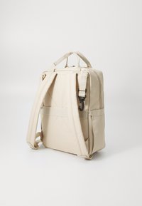 Sac à dos beige avec des bretelles réglables, dos matelassé, poignée supérieure et crochet. Présente un design rectangulaire simple et un tissu texturé robuste.