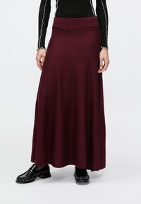 Fustă maxi burgundă din material moale, cu talie bine definită și design fluid. Asortată cu pantofi negri lucioși.