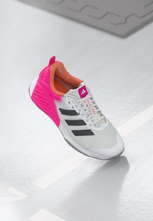 Baskets blanches Adidas avec des bandes noires, talon rose vif et doublure intérieure orange, sur un sol gris clair.