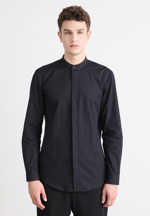 Camisa negra de manga larga con cuello mao, cierre de botones y textura suave. Ajuste entallado y bajo redondeado para un aspecto estructurado.