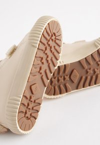 Beige children's shoes with a textured rubber sole and Velcro strap. The sole features distinct tread patterns, including star shapes.