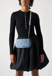 Κουβερτίνα ανοιχτού μπλε χρώματος τσάντα με ασημί αξεσουάρ, φορεμένη χιαστί, σε συνδυασμό με μαύρο ραμμένο μακρυμάνικο φόρεμα και μαύρη φαρδιά φούστα.