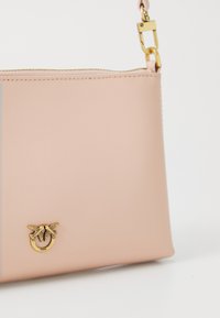 Rozā ādas crossbody soma ar zelta furnitūru, kas piedāvā dekoratīvu piespraudi un rāvējslēdzēju augšpusē. Gluda tekstūra, minimālisma dizains.
