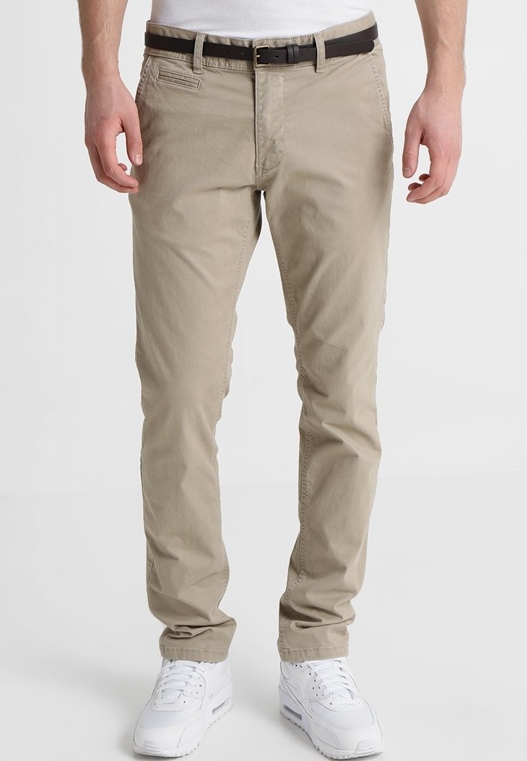Beige Chinos aus Baumwolle in schmaler Passform. Mit einem Reißverschluss, fünf Taschen und einem braunen Leder-Gürtel ausgestattet. Werden mit weißen Sneakers getragen.