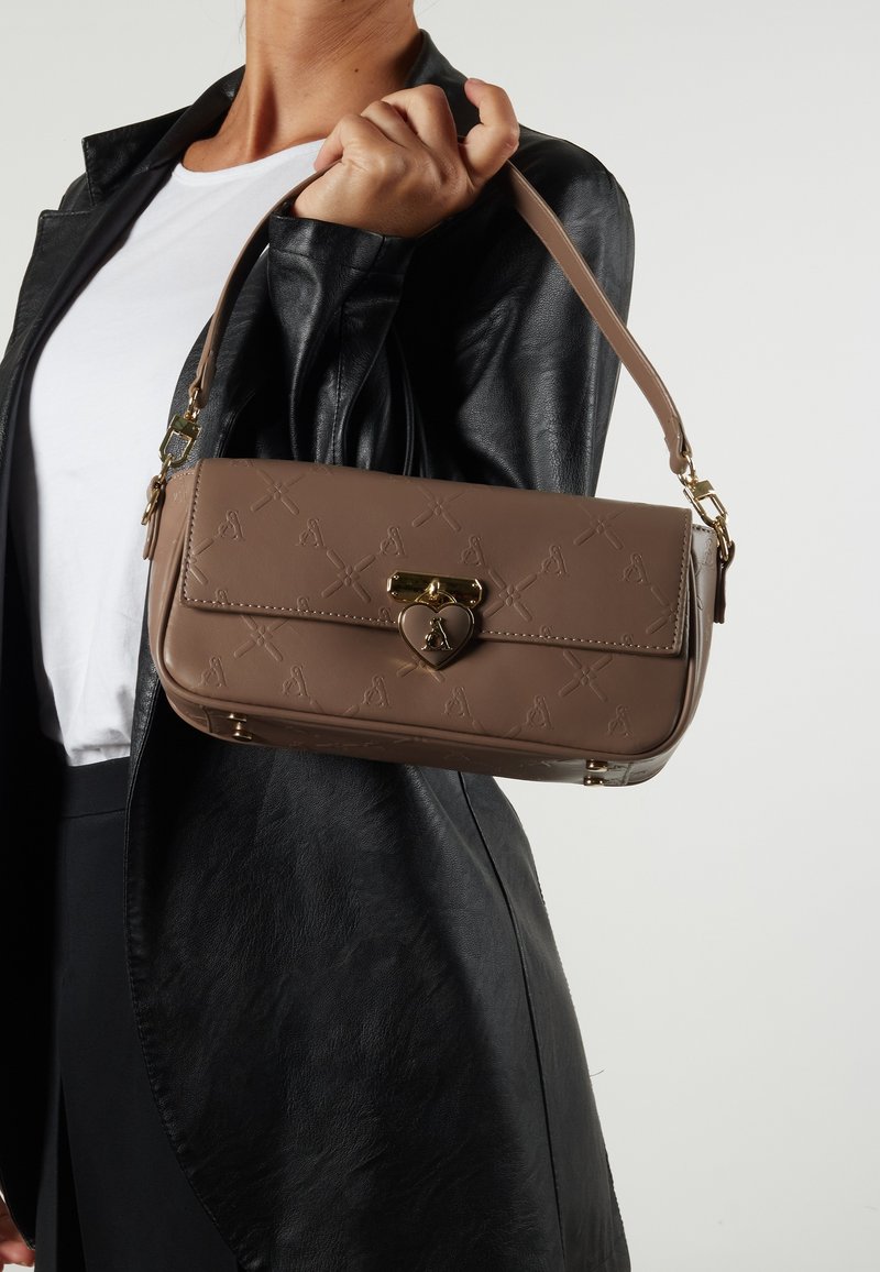 Brown faux leather handbag with embossed patterns, a heart-shaped clasp, and a single handle, shown against a black leather jacket.