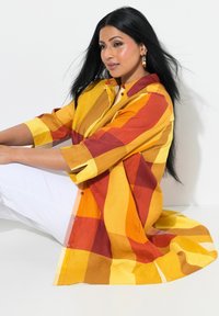 Camicia a quadri colorata in giallo, arancione e bordeaux, realizzata in tessuto leggero con chiusura a bottoni e maniche a tre quarti.