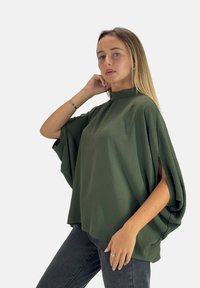 Maglietta verde oversize con un collo alto, maniche corte e un tessuto testurizzato. Abbinata a jeans grigi scuri.