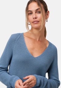 Lichtblauwe gebreide trui met een diepe V-hals, geribbelde textuur en lange mouwen. Bevat licht afgezakte schouders en aansluitende manchetten.