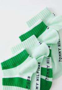 Zaļi un balti svītroti zeķes, kas izgatavotas no mīksta auduma ar ribotām malām; sānos ir logo teksta uzraksts tumši zilā krāsā, parādītas trīs pāri.