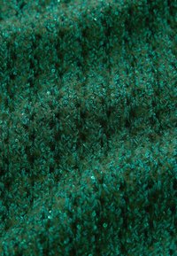 Tissu tricoté vert avec un motif texturé, présentant des accents en fil brillant et une apparence douce et duveteuse.
