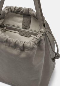 Bolso de cuero gris en forma de cubo con parte superior gathered, cordón ajustable y bolsillo interior con cremallera. Presenta un logotipo sutil y una textura suave.