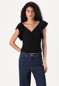 Svart kortermet topp med V-hals og volanger på skuldrene; teksturert stoff; tettsittende silhuett; kombinert med høyt liv mørke denim jeans.