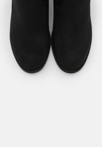 Bottines en daim noir avec un bout arrondi, des coutures apparentes le long de la semelle et une texture lisse. Vue de dessus mettant en valeur le design.