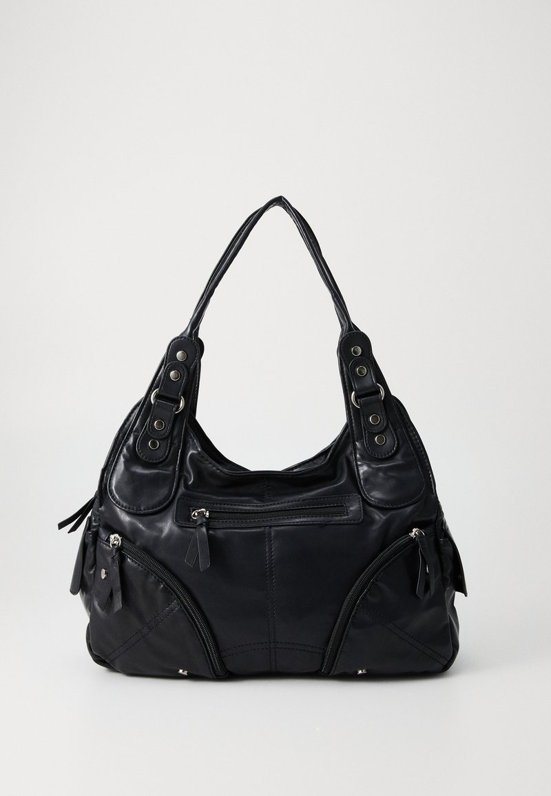 Bolsa de mão de couro preto com alças duplas, bolsos frontais com fecho éclair e detalhes em rebites metálicos, colocada sobre um fundo liso claro.