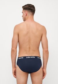 Sötétkék alsónadrág lágy elasztikus derékkal, amelyen fehér "Levi's" felirat található. Simaság, klasszikus alsónadrág dizájn, minimális kiegészítők.