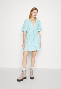 Robe mini en coton bleu clair avec des manches bouffantes, des détails en œillets, un décolleté en V et une taille à cordon, associée à des bottes chelsea à lacets beige.