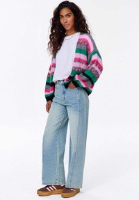 Barevný pletený cardigan s pruhy v růžové, zelené a šedé barvě. Kombinován s světle modrými širokými džíny a hnědými teniskami s růžovými pruhy.