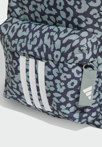 Mochila con un patrón de leopardo en azul oscuro y verde azulado claro. Presenta tres franjas blancas y una pequeña etiqueta gris con un logo. Tela texturizada.