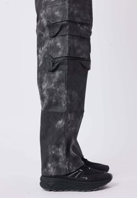 Schwarze Cargo-Hosen mit einer strukturierten, marmorierten Oberfläche. Verfügt über mehrere Seitentaschen und ist kombiniert mit schwarzen Sneakers mit geschichteten Sohlen.