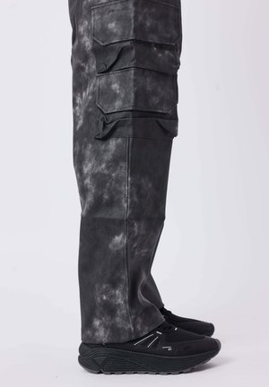 Pantalones cargo negros con un acabado texturizado y moteado. Presenta múltiples bolsillos laterales y se combina con zapatillas negras de suela en capas.