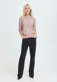 Pull polo rose clair à manches courtes avec un col et trois boutons, associé à un jean droit noir et des escarpins noirs pointus.