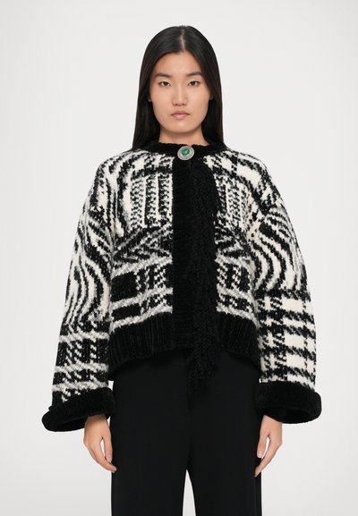 Cardigan à motifs noir et blanc avec une finition texturée, fermeture à bouton rond vert et manches oversized. Poignets et ourlet côtelés.