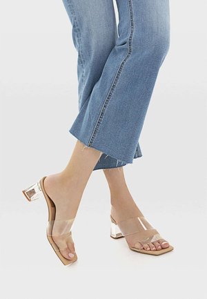Sandales à talons transparents avec deux brides transparentes et un bout carré. Le talon est épais et transparent, associé à une semelle beige.