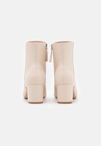 Beżowe skórzane botki na kostkę z blokowym obcasem i zamkiem błyskawicznym z boku. Gładka tekstura z minimalnymi detalami szycia. Okrągły kształt czubka.