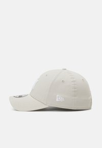 Casquette de baseball en tissu beige clair avec logo et accents brodés blancs. Elle dispose d'une couronne structurée, d'une visière courbée et de trous de ventilation.